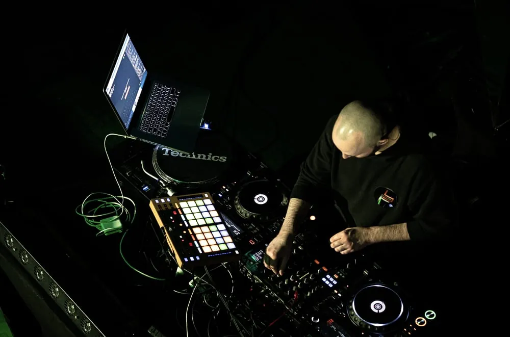 Blick von oben auf Bornd Fono beim Mixen in einem dunklen Club, vor ihm Technics-Plattenspieler, CDJs und ein Laptop